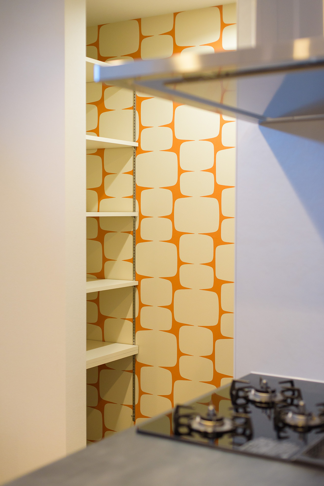 さらに無彩色でまとめられた空間の中に、ご夫婦で選んだオレンジ色のアクセントクロスをパントリーに採用し...